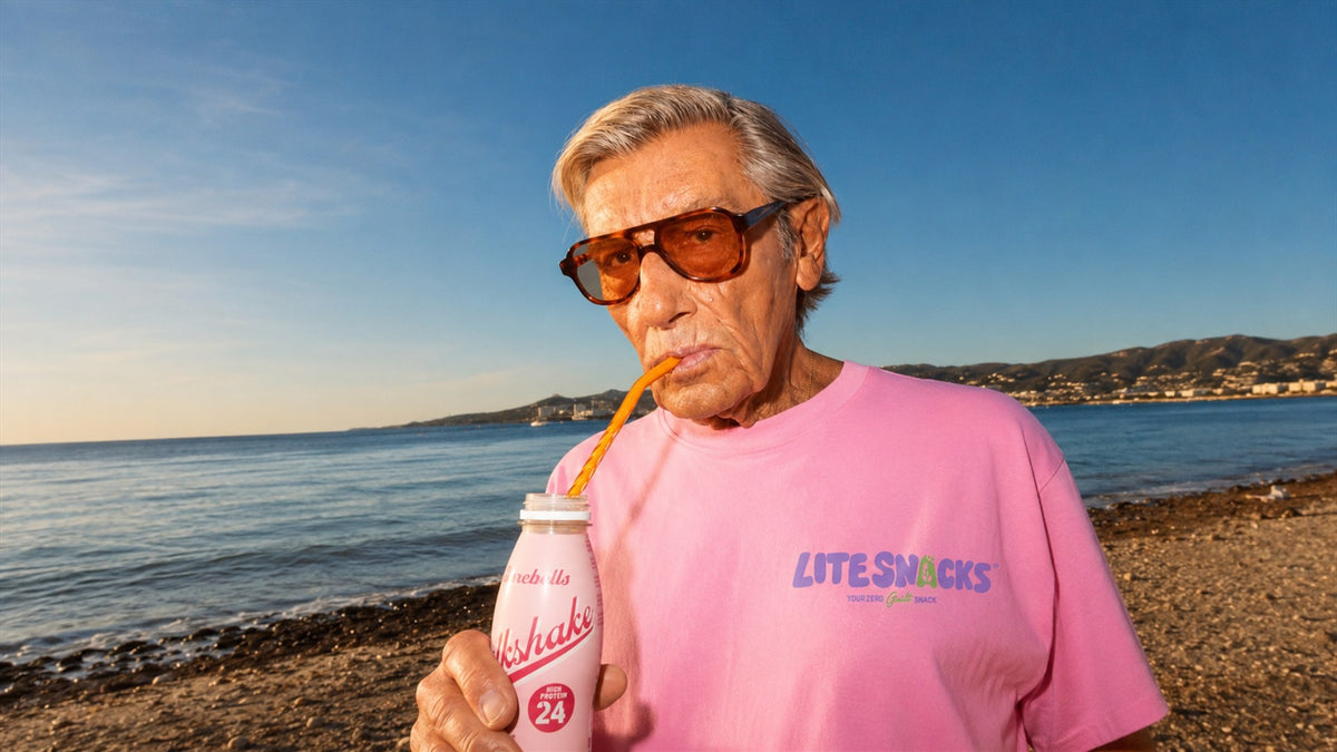 Man on a beach in a pink Lite Snacks t-shirt drinking a high-protein milkshake